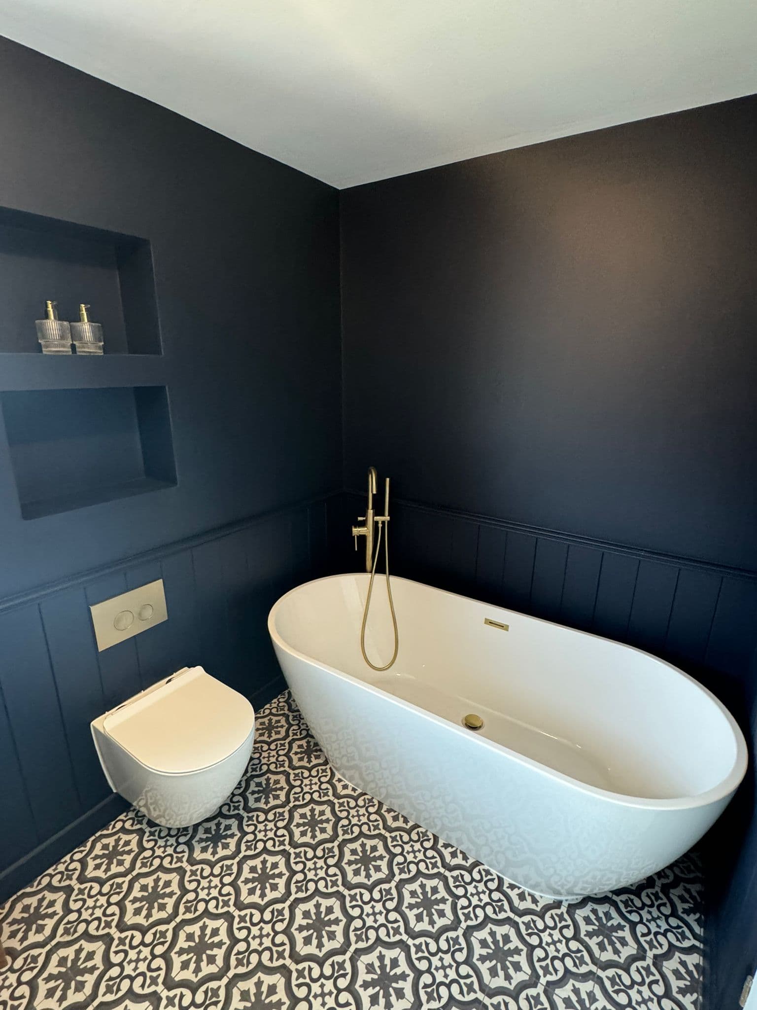 Navy panelled bathroom with a freestanding bath and brushed brass floor mounted tap