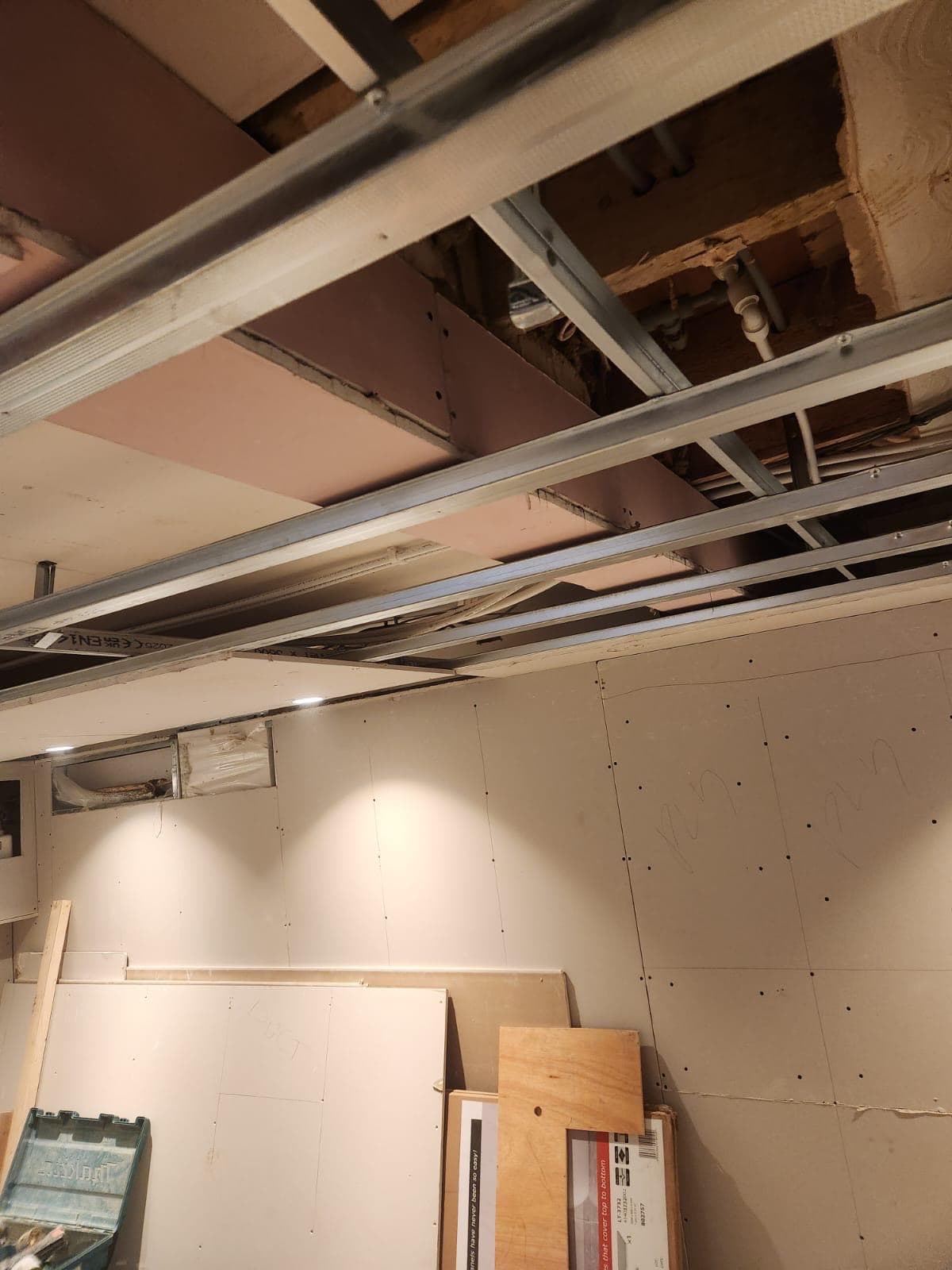 Metal ceiling framing in the basement with pipework and cabling run through before the plasterboard goes on