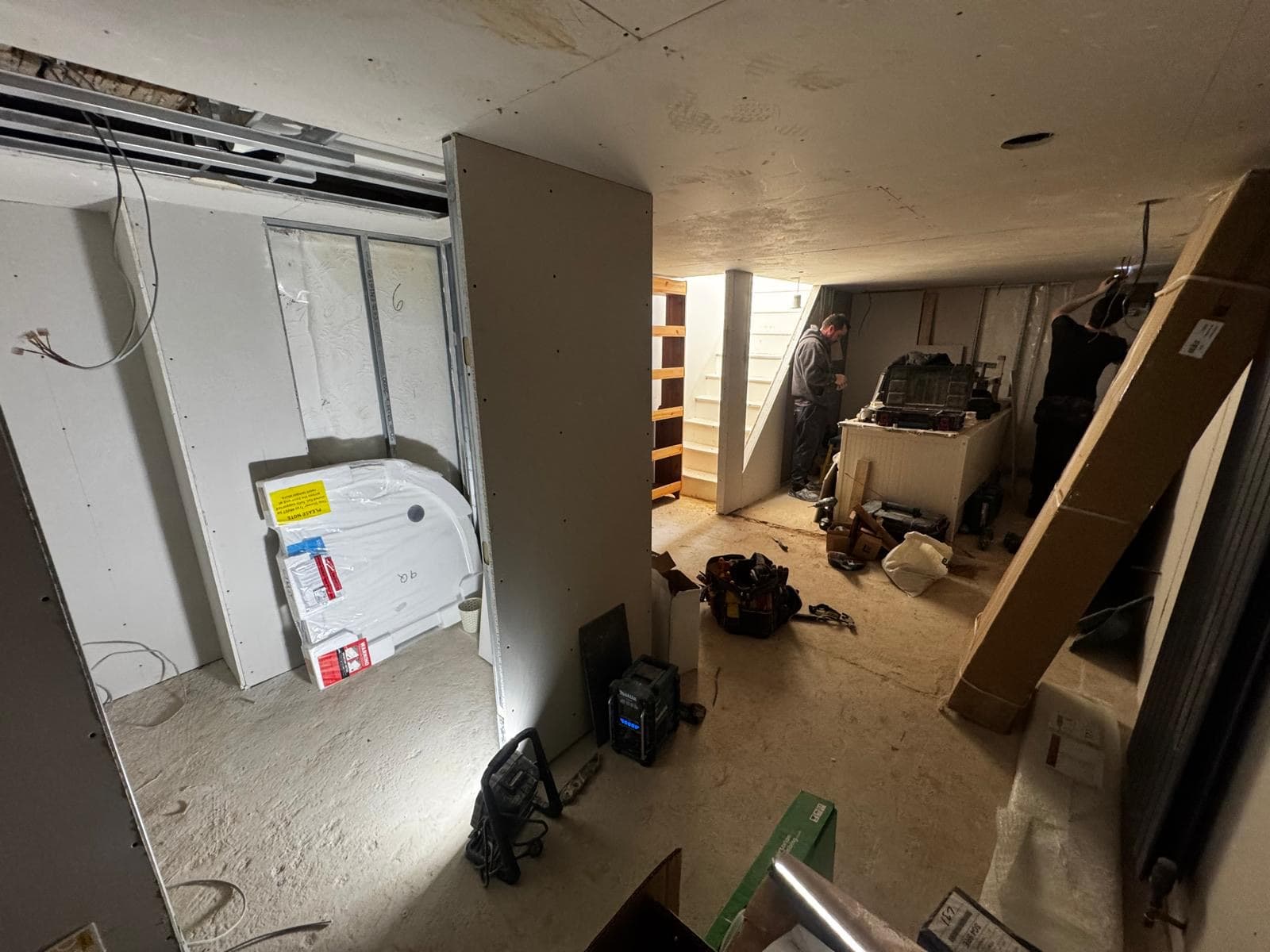 Shower room studded out in the corner of the basement with the tray still wrapped and the team working on the walls behind