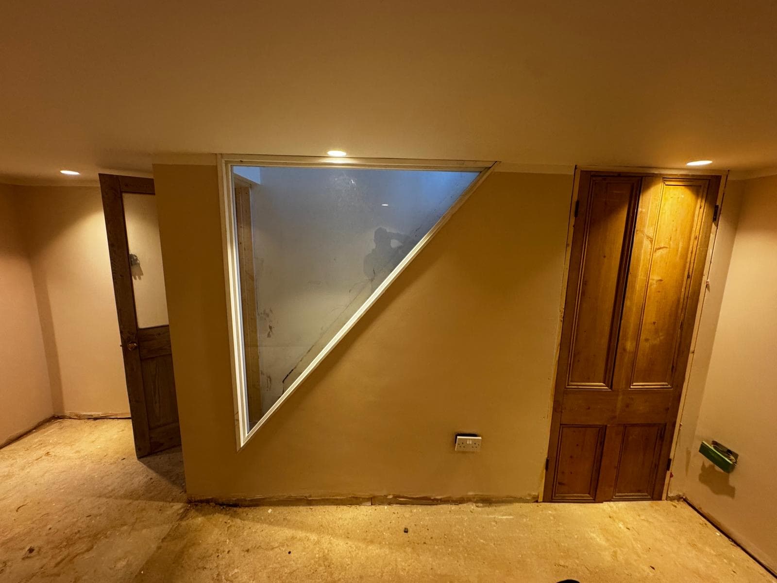Freshly plastered basement wall with the triangular stairwell window framed in and the original panelled doors rehung
