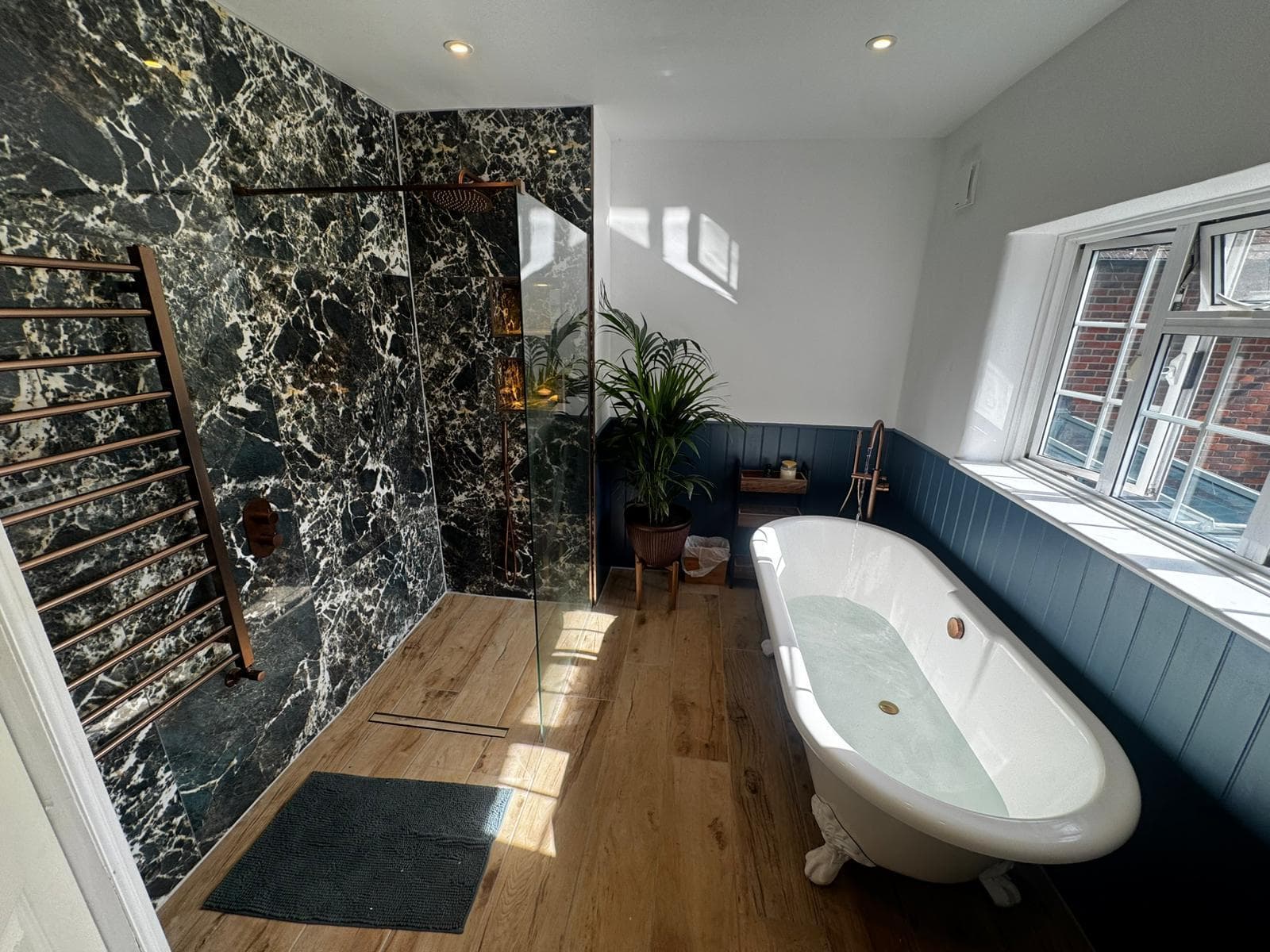 Green marble wet room in Stevenage with a copper rainfall shower, roll-top clawfoot bath, navy panelling and warm oak effect flooring