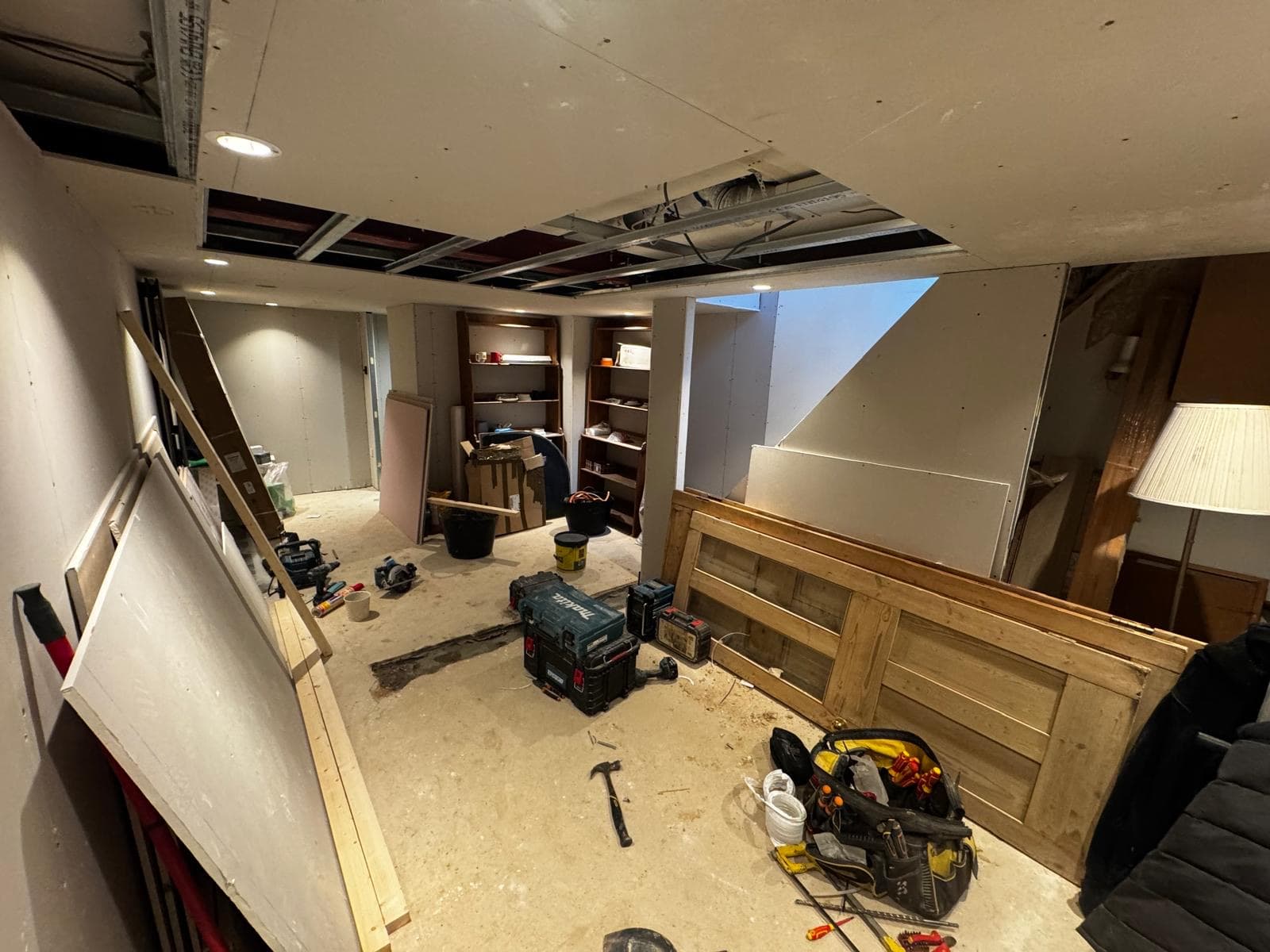 Stevenage basement stripped back, with the ceiling opened up, tools across the floor and original timber doors stacked against the wall