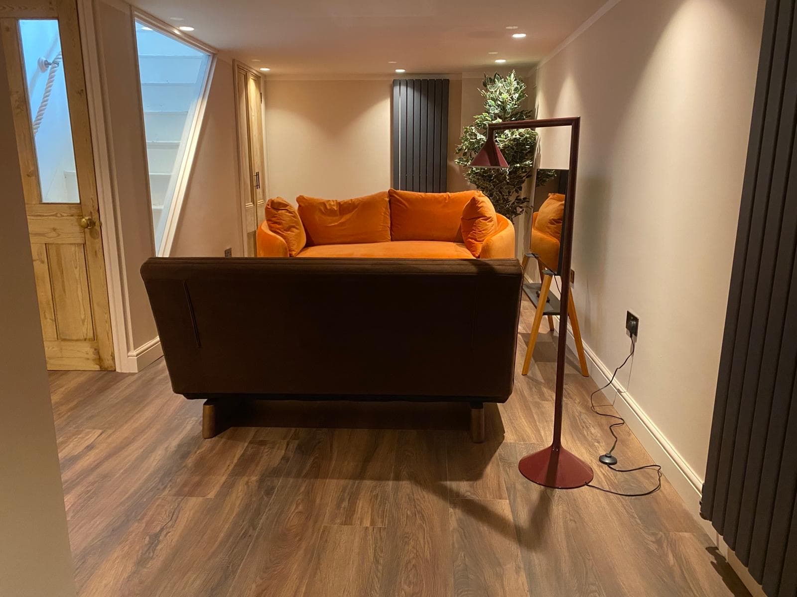 Finished basement snug with an orange velvet sofa, wood effect flooring and the stairwell window letting light through