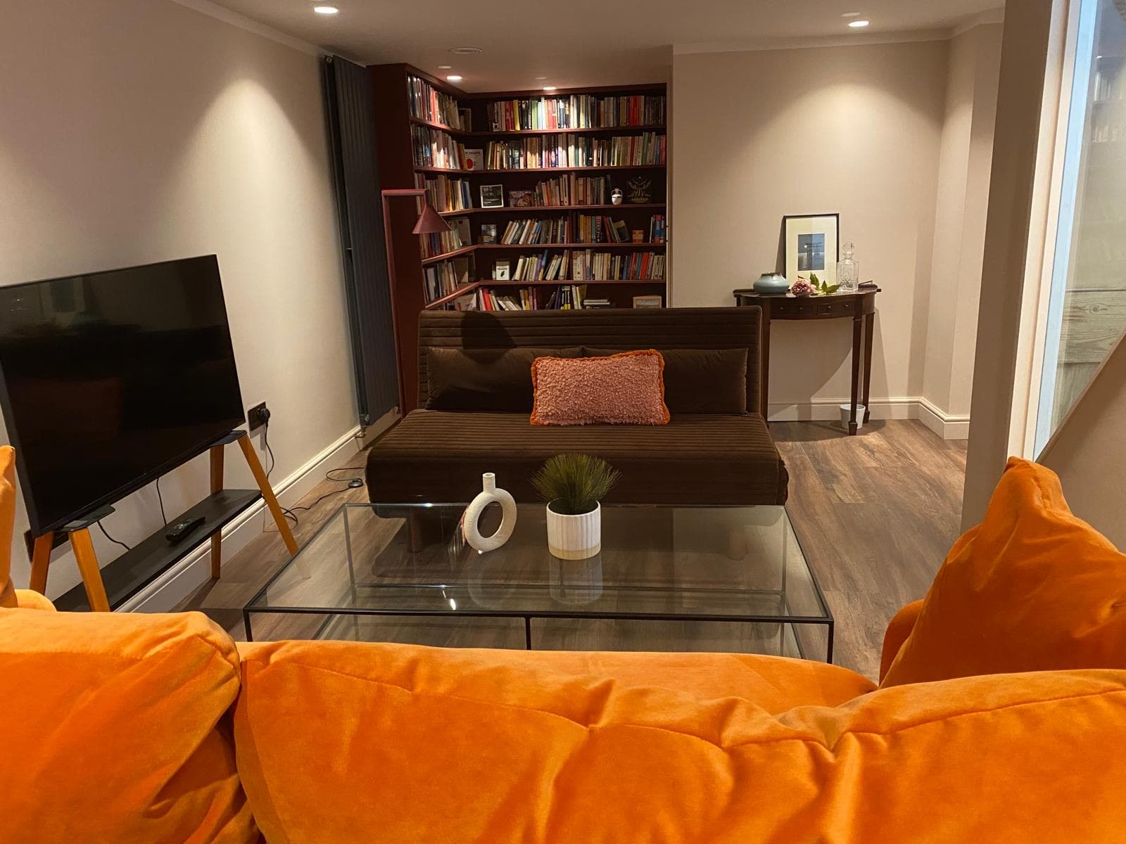 Finished basement lounge with a wall mounted television, bookcase, glass coffee table and vertical radiators